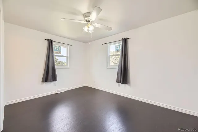 an empty room with wooden floor chandelier fan and windows