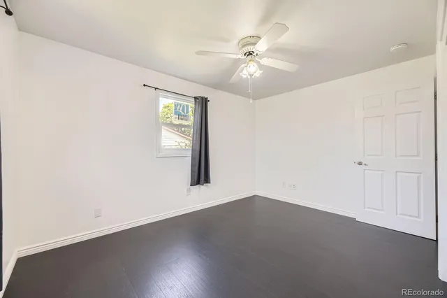 an empty room with wooden floor chandelier fan and windows