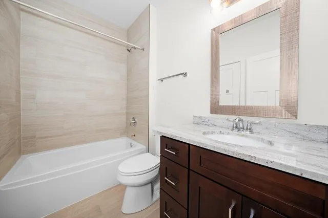 a bathroom with a granite countertop bathtub shower sink vanity mirror and toilet