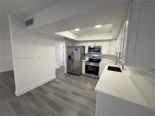 an empty room with wooden floor kitchen view and a window