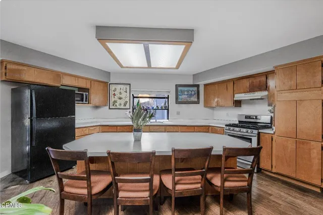 a kitchen with stainless steel appliances a sink a stove a refrigerator a dining table and chairs