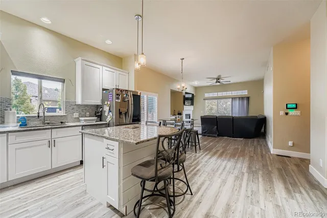 a open kitchen with stainless steel appliances granite countertop a stove top oven a refrigerator a sink and white cabinets with wooden floor