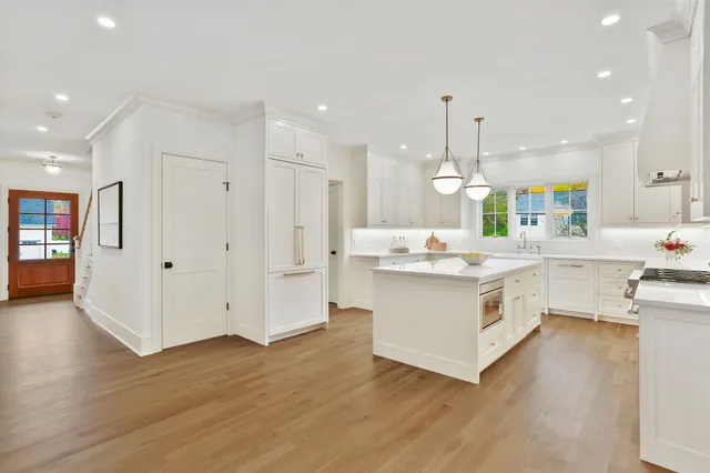 a large white kitchen with kitchen island a chandelier stainless steel appliances cabinets and wooden floor