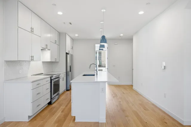 a large kitchen with stainless steel appliances a large counter top a stove and a wooden floors