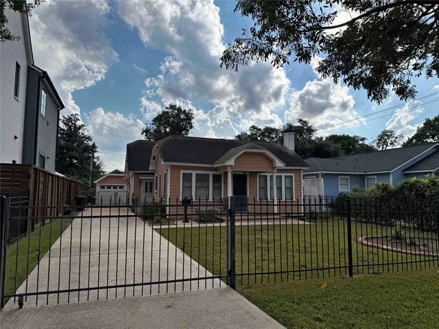 a view of a brick house with a small yard plants and large trees