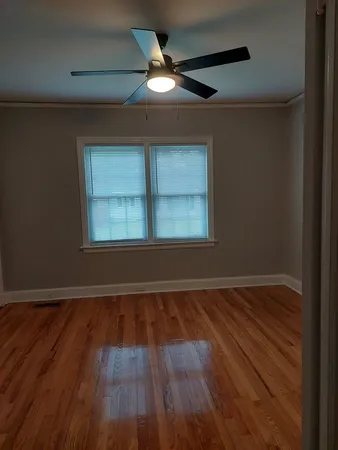 an empty room with wooden floor chandelier fan and windows