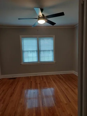 an empty room with wooden floor chandelier fan and windows