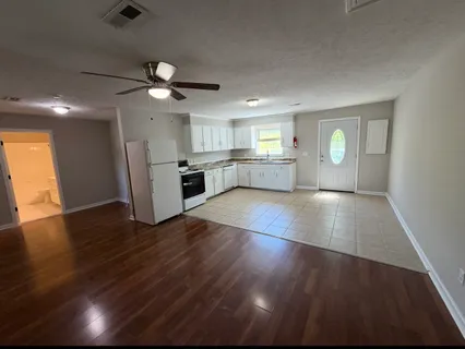an empty room with wooden floor a ceiling fan and kitchen view