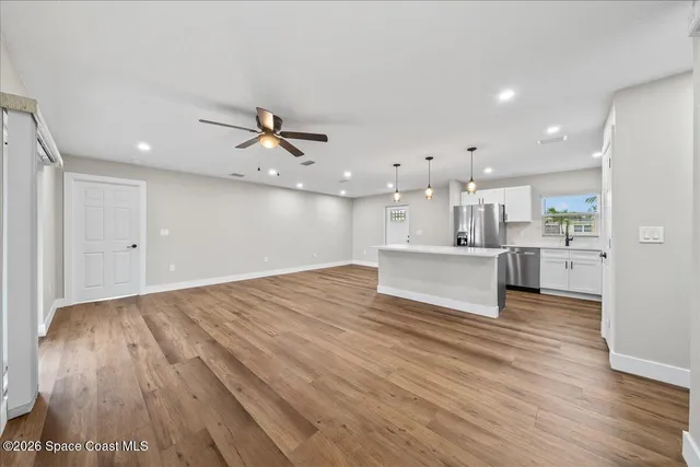 a view of an empty room with wooden floor and a kitchen