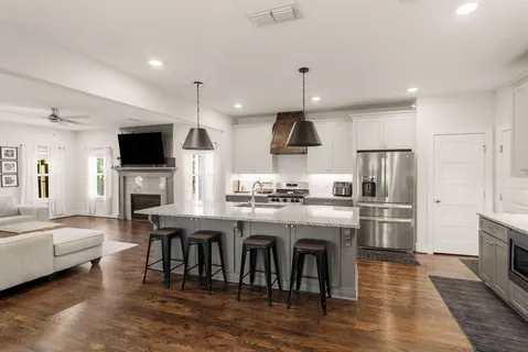 a kitchen with stainless steel appliances a kitchen island a stove a refrigerator a oven a sink a dining table and chairs with wooden floor