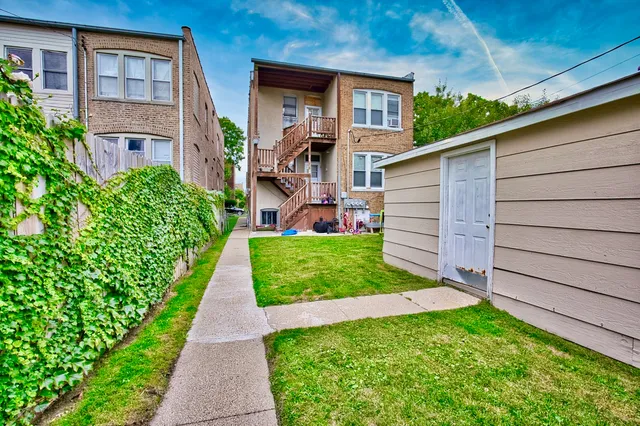 a view of a brick house with a yard plants and large tree