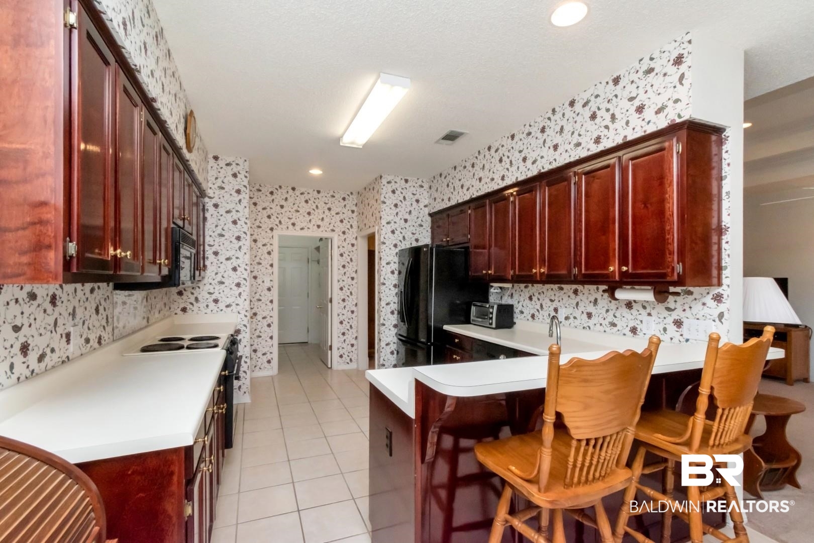 1032 Cross Gates Place Mobile, AL 36609 - Photo 10 of 34 Kitchen with light countertops, light tile patterned flooring, black appliances, a kitchen breakfast bar, and bold wood finish cabinetry