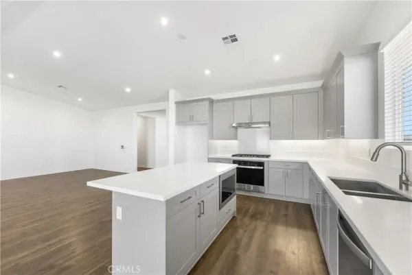 a large white kitchen with a stove top oven a sink a refrigerator and white cabinets with wooden floor