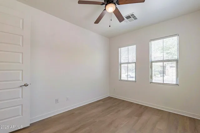 an empty room with wooden floor chandelier fan and windows