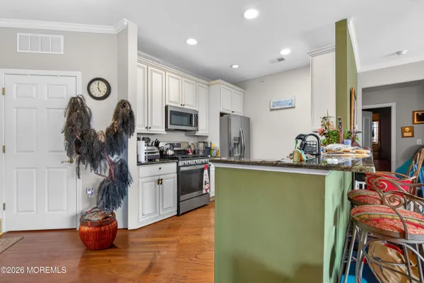 a kitchen with stainless steel appliances granite countertop a refrigerator a stove top oven a sink dishwasher and white cabinets with wooden floor