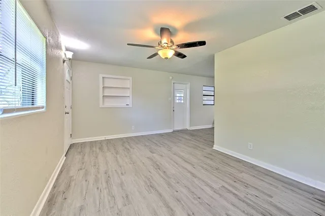 an empty room with wooden floor chandelier fan and windows