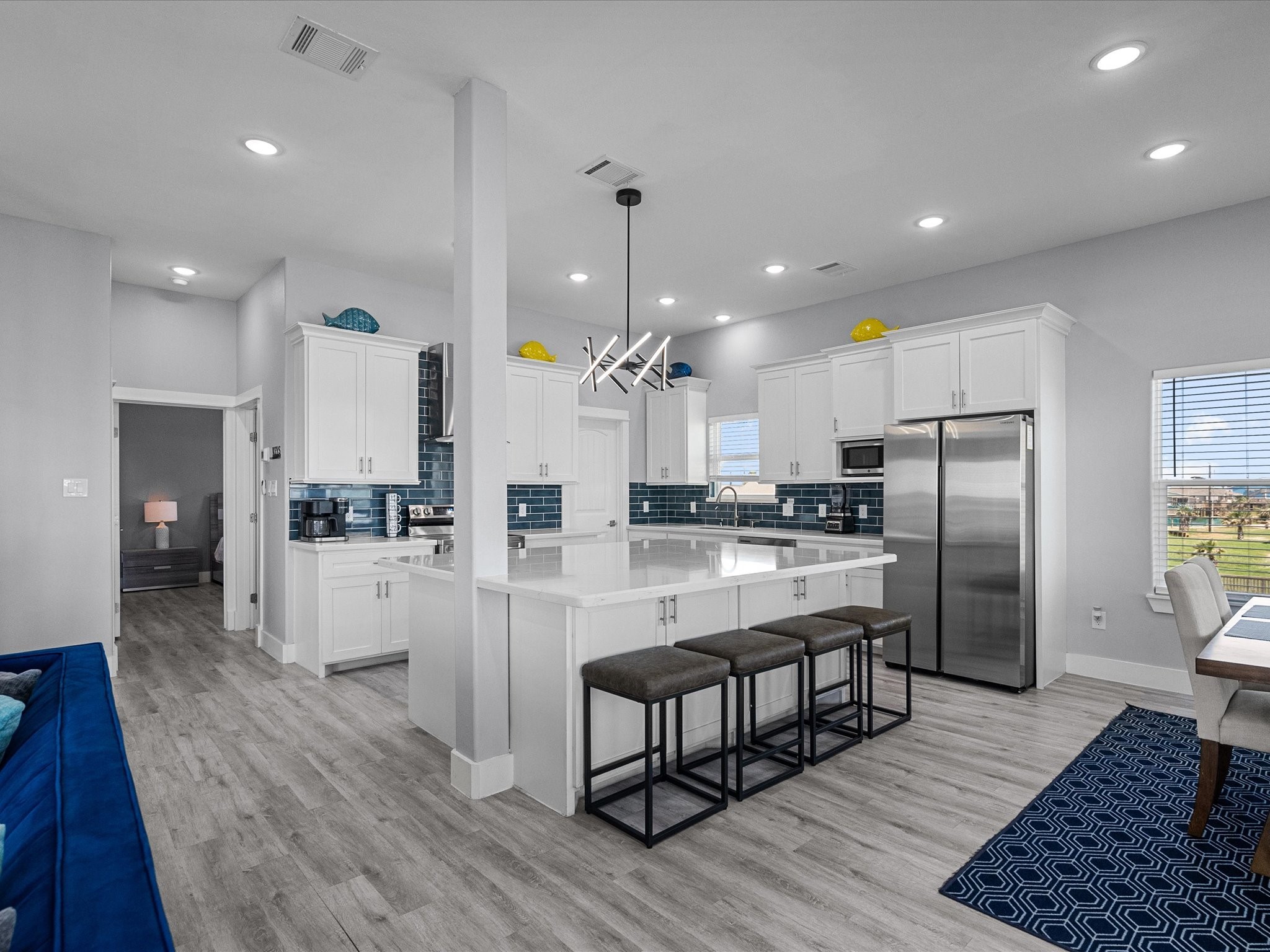 718 Beach Drive Surfside Beach, TX 77541 - Photo 15 of 49 This modern kitchen boasts sleek white cabinetry, stainless steel appliances, and a striking blue tile backsplash. It's bright, airy, and offers ample counter space with plenty of natural light.