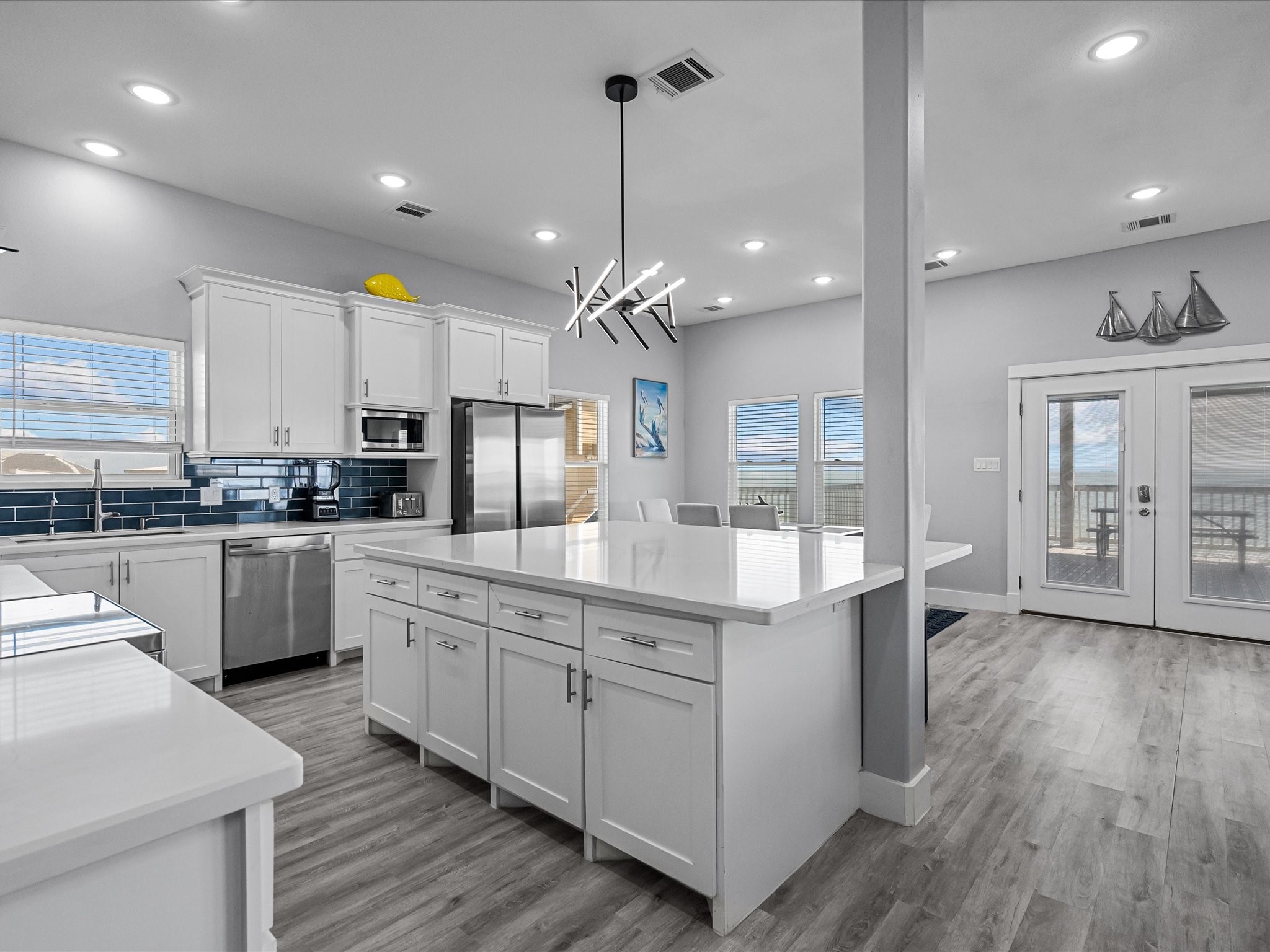 718 Beach Drive Surfside Beach, TX 77541 - Photo 16 of 49 Experience the elegance of this modern kitchen, featuring sleek white cabinetry, a spacious island, stainless steel appliances, and a striking blue tile backsplash.