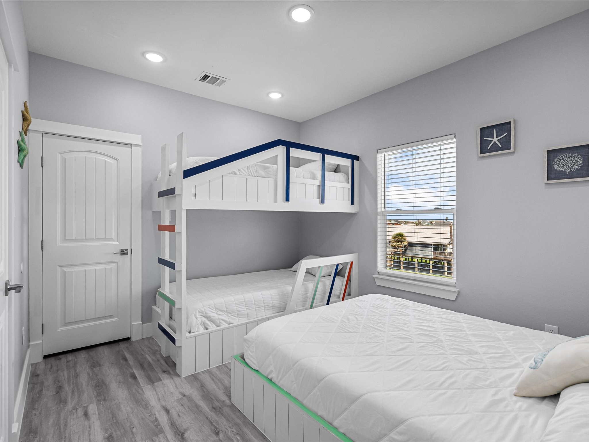718 Beach Drive Surfside Beach, TX 77541 - Photo 38 of 49 Bright and inviting bedroom with modern gray walls and flooring, featuring two colorful bunk beds. Enjoy ample natural light and outdoor views through large windows and a glass door.