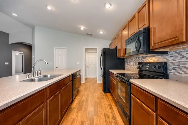 a kitchen with stainless steel appliances granite countertop a sink a stove top oven a refrigerator with wooden cabinets and floor