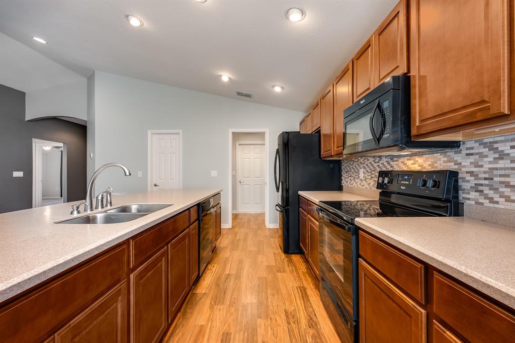 1355 Windward Oaks Loop Auburndale, FL 33823 - Photo 4 of 25 a kitchen with stainless steel appliances granite countertop a sink a stove top oven a refrigerator with wooden cabinets and floor