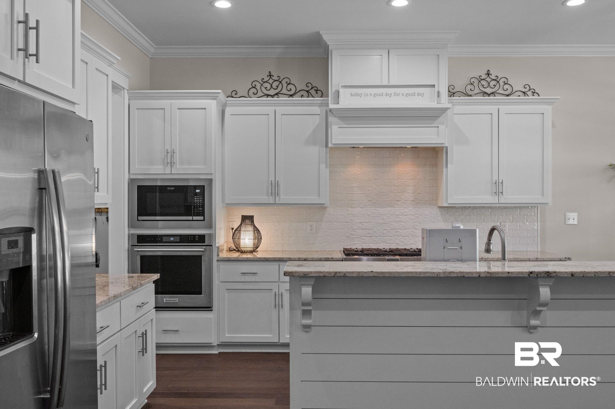 32194 Badger Court Daphne, AL 36527 - Photo 15 of 49 Kitchen featuring stainless steel appliances, white cabinetry, light stone counters, crown molding, and dark wood finished floors