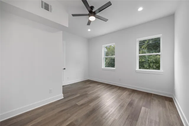 an empty room with wooden floor ceiling fan and windows