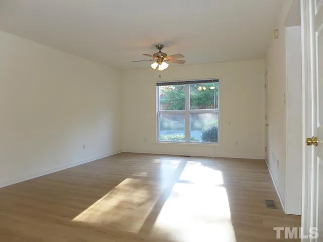 an empty room with wooden floor chandelier fan and windows