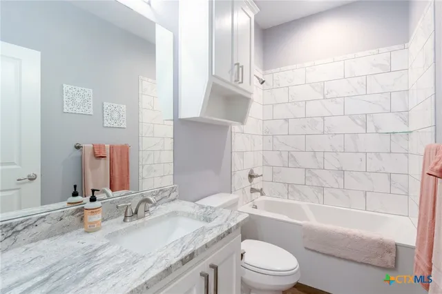 a bathroom with a granite countertop bathtub shower sink vanity mirror and toilet