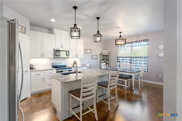 a kitchen with stainless steel appliances kitchen island granite countertop a table chairs and a refrigerator