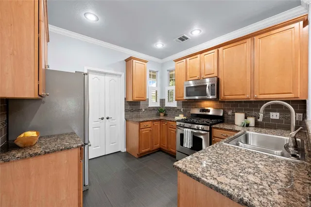 a kitchen with stainless steel appliances granite countertop a stove top oven a sink dishwasher and a refrigerator with wooden floor