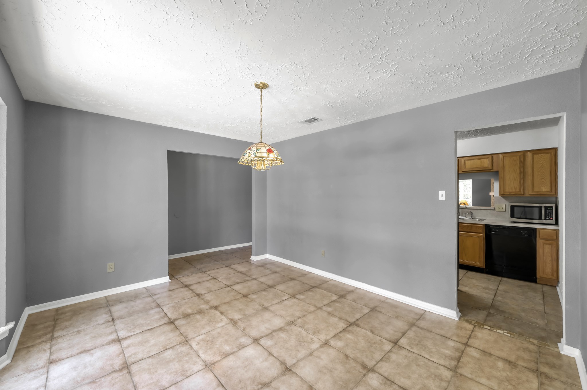 4314 Enchantedgate Drive Spring, TX 77373 - Photo 8 of 47 This room features neutral gray walls and a tiled floor, creating a clean, modern space. A decorative pendant light hangs from the ceiling, and two doorways lead to other areas, with one showing a glimpse of a kitchen with wooden cabinets.