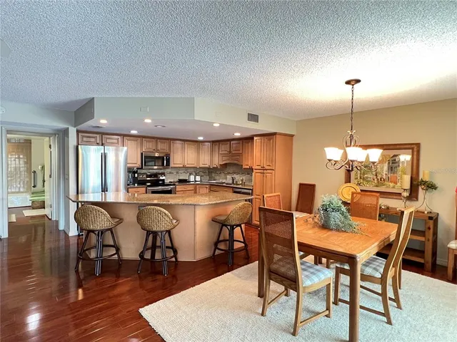 a dining room with stainless steel appliances kitchen island granite countertop a dining table chairs and a refrigerator