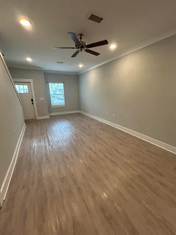 an empty room with wooden floor a ceiling fan and windows