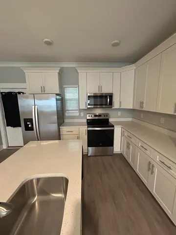 a kitchen with stainless steel appliances granite countertop a sink a stove a refrigerator with white cabinets and wooden floor