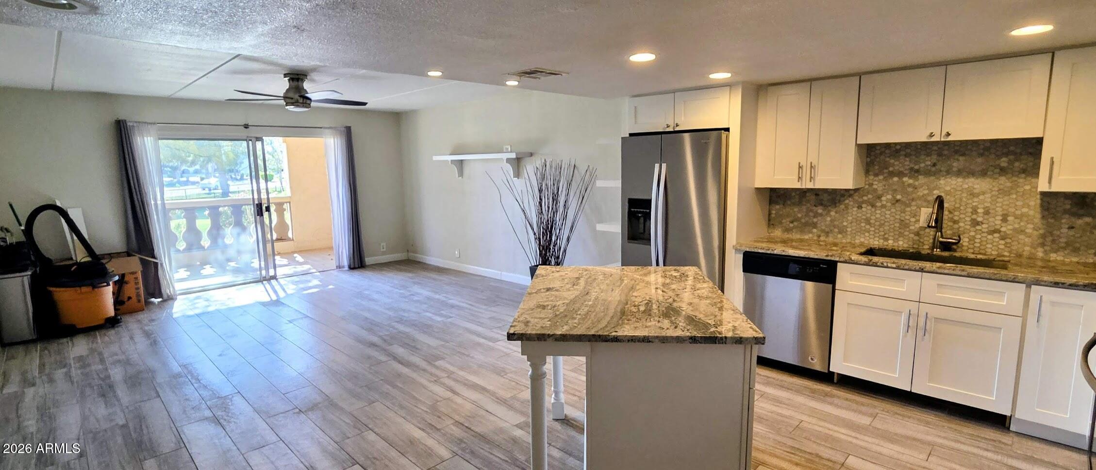 7910 East Camelback Road, Unit 104 Scottsdale, AZ 85251 - Photo 30 of 38 a kitchen with kitchen island granite countertop wooden floors white cabinets and stainless steel appliances