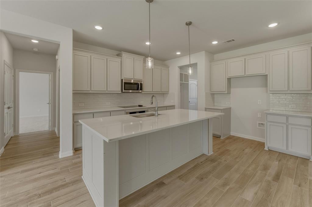 156 Oak Grv Way Springtown, TX 76082 - Photo 11 of 25 Kitchen featuring a large central island with an integrated sink, light-toned cabinetry, light countertops, subway tile backsplash, and wood-finish flooring