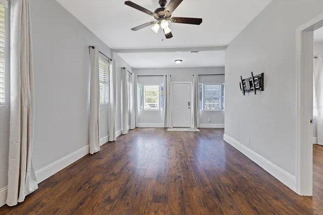 an empty room with wooden floor ceiling fan and windows