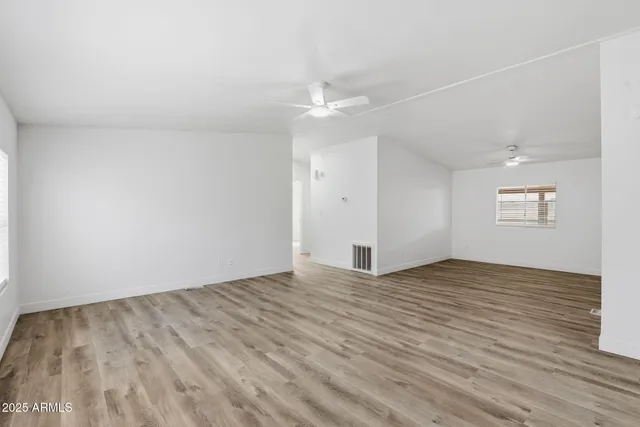 an empty room with wooden floor chandelier fan and windows
