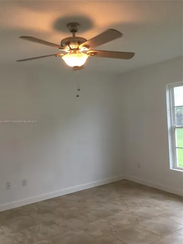 an empty room with a chandelier fan and windows