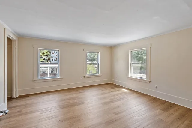 a view of an empty room with wooden floor and window