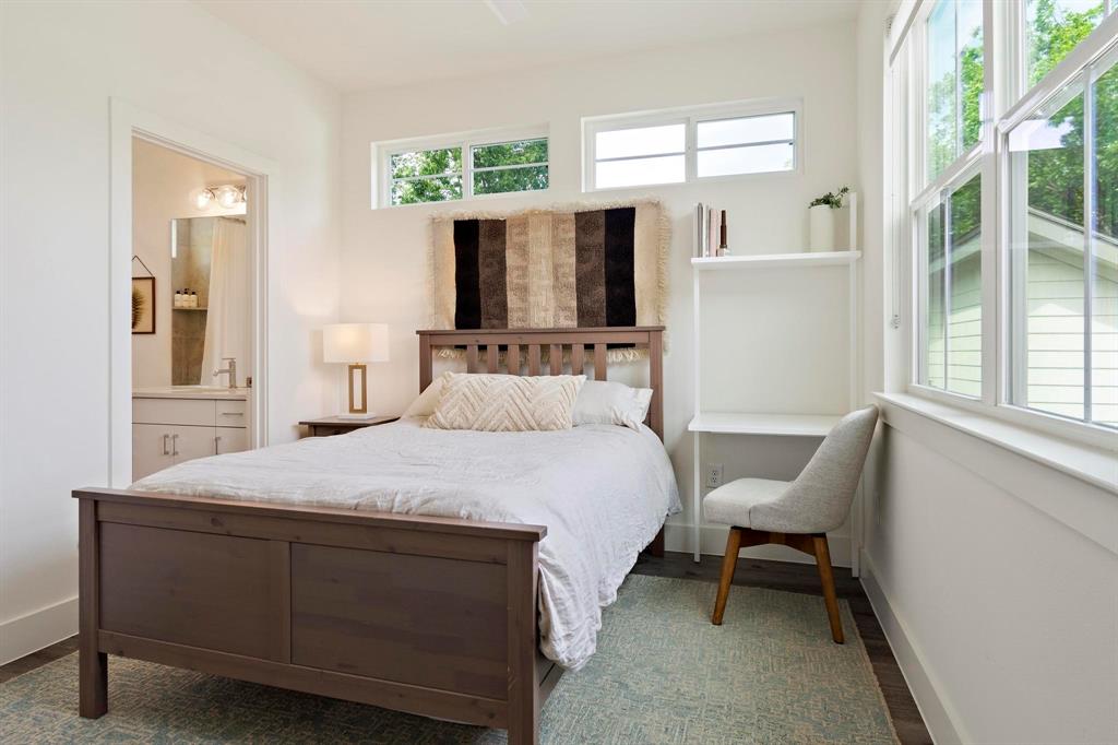 911 Stobaugh Street, Unit 2 Austin, TX 78757 - Photo 19 of 26 Bright bedroom featuring large windows, a built-in desk with shelving, wood-finish flooring, and direct access to a bathroom with a vanity and modern fixtures
