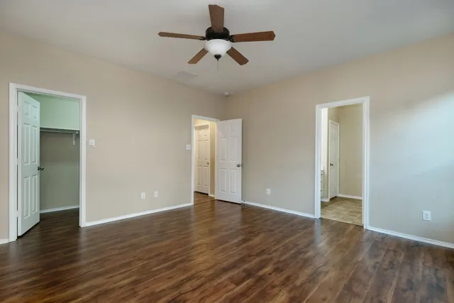 an empty room with wooden floor ceiling fan and windows