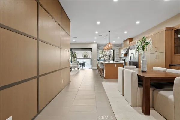 a dining hall with stainless steel appliances granite countertop a refrigerator a oven a kitchen island a couches and a dining table with wooden floor