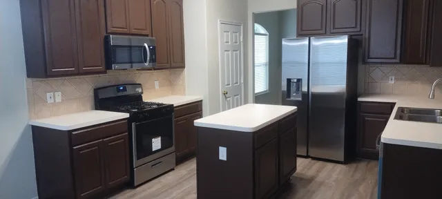 a kitchen with stainless steel appliances granite countertop a refrigerator a sink a stove and wooden cabinets