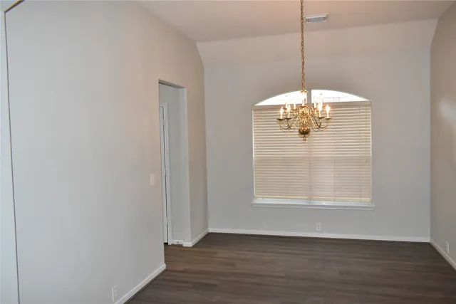 a view of an empty room with wooden floor and chandelier