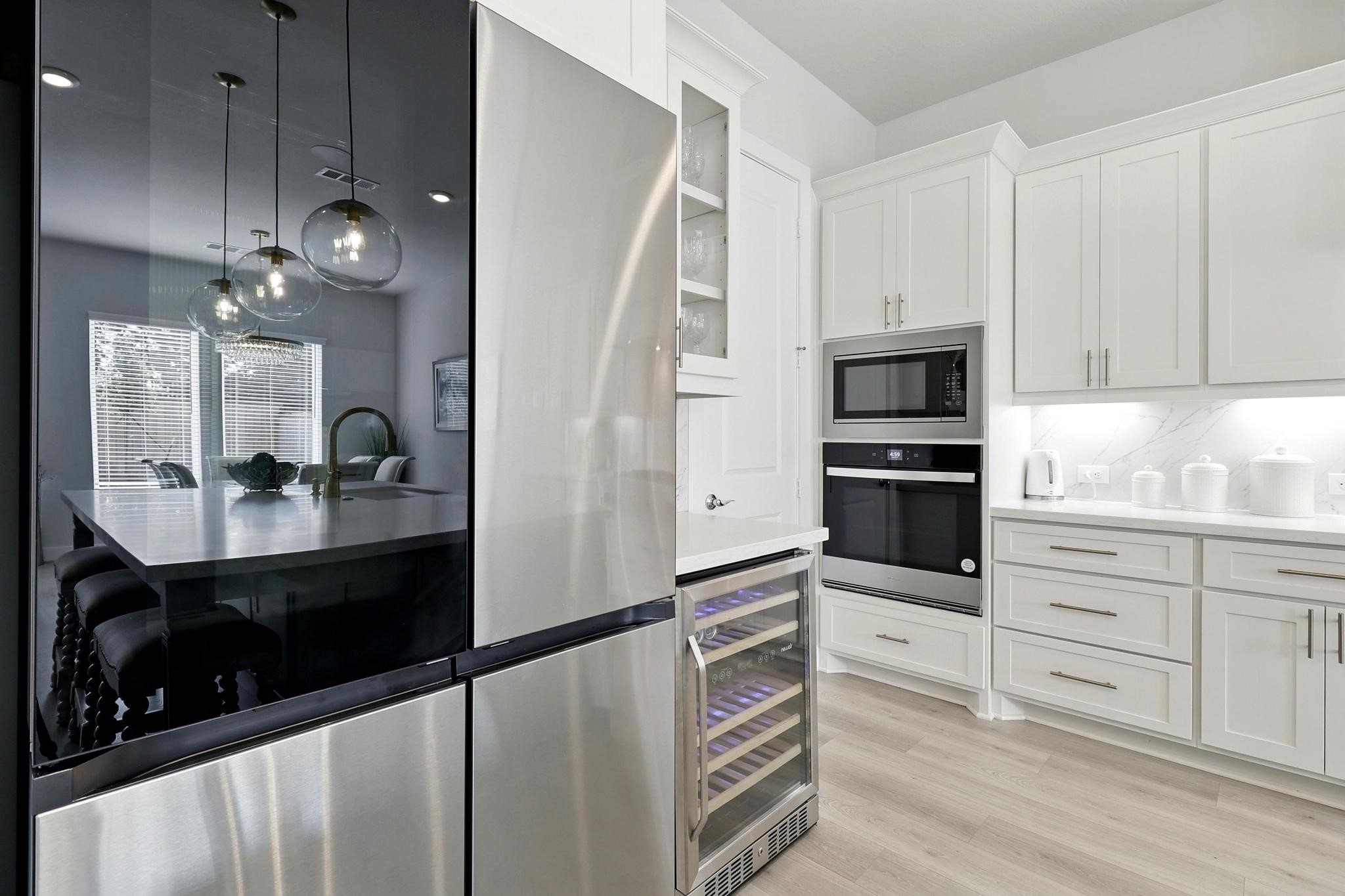 26923 Arethusa Court Spring, TX 77389 - Photo 7 of 44 Modern kitchen with sleek stainless steel appliances, bright white cabinetry, and light wood flooring. Features a built-in wine cooler and double oven, with ample counter space and elegant pendant lighting over the dining area.