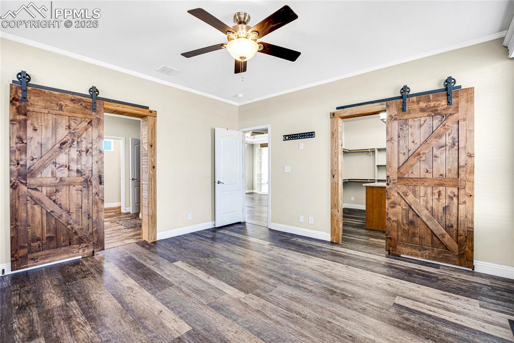 7880 J D Johnson Road Peyton, CO 80831 - Photo 9 of 50 Unfurnished bedroom featuring a barn door, a walk in closet, ornamental molding, ceiling fan, and wood finished floors