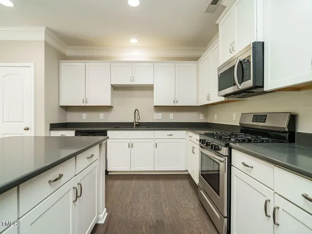 a kitchen with stainless steel appliances granite countertop grey cabinets a stove a sink and a microwave
