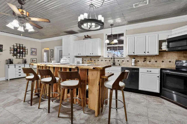 a kitchen with stainless steel appliances kitchen island granite countertop a dining table chairs and a refrigerator